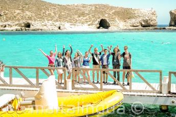 A group of studenți waving next to a boat at the Blue Lagoon, Comino