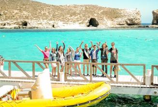 A group of studenți waving next to a boat at the Blue Lagoon, Comino